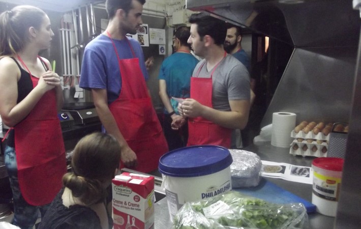 Várias pessoas de avental vermelho, numa cozinha em atividade de Team cooking.